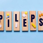 The word EPILEPSY is written on wooden blocks on a blue background near the pills.